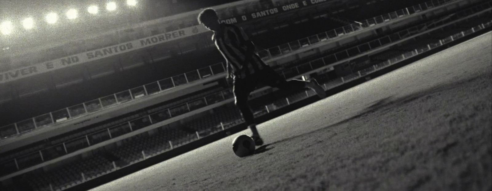 Futbolista conduciendo el balón en un estadio vacío, de noche